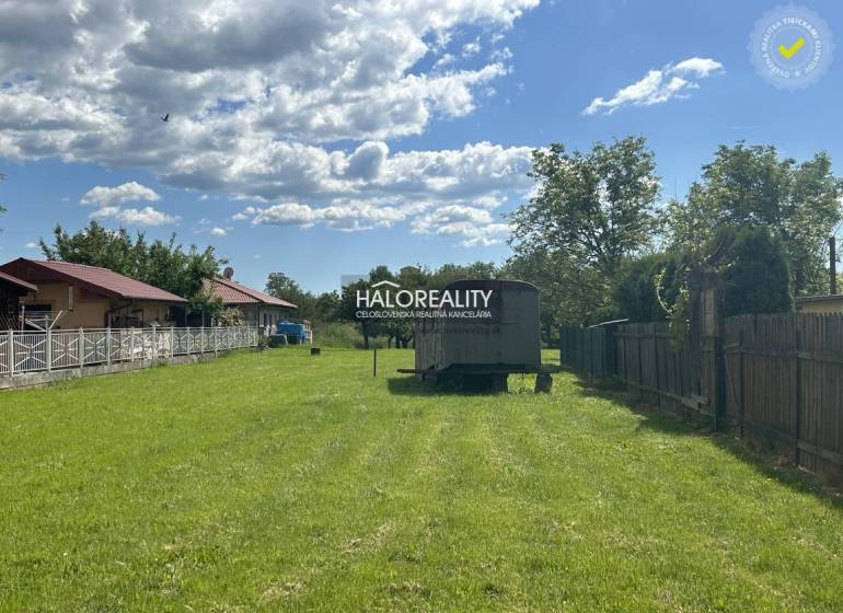 A green plot in the village with the possibility of living, between fences and with a trailer.