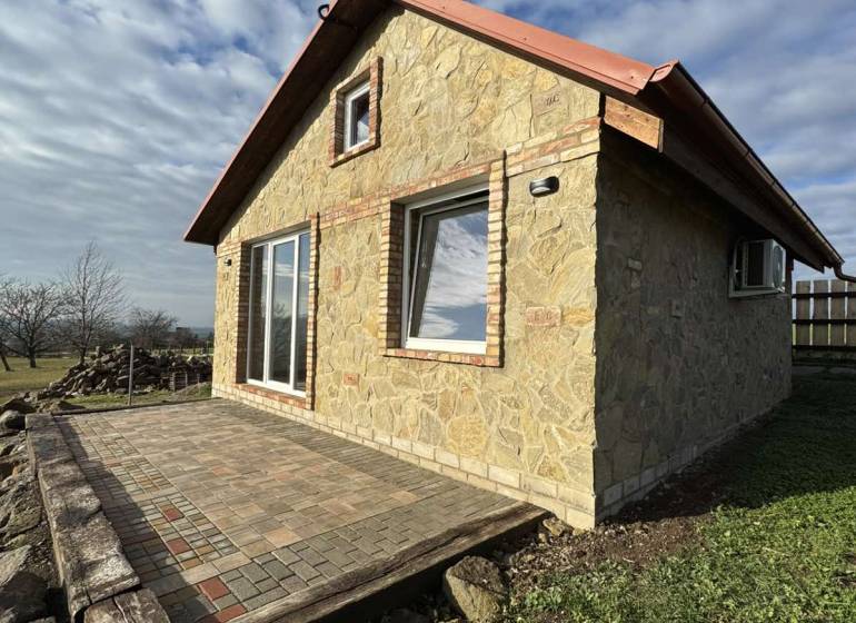 Stone cottage in Šahy with a terrace, surrounded by nature and a blue sky.