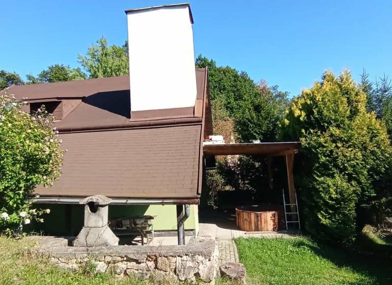A cottage in Ružiná surrounded by greenery, outdoor seating, and a stone fireplace.