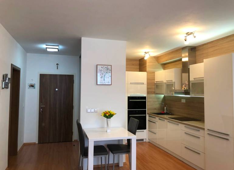 A kitchen with white furniture and a dining table in a 2-room apartment, flooring with a wooden decor.