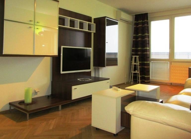 Living room with a TV and white sofas, wooden decor flooring in a two-room apartment.