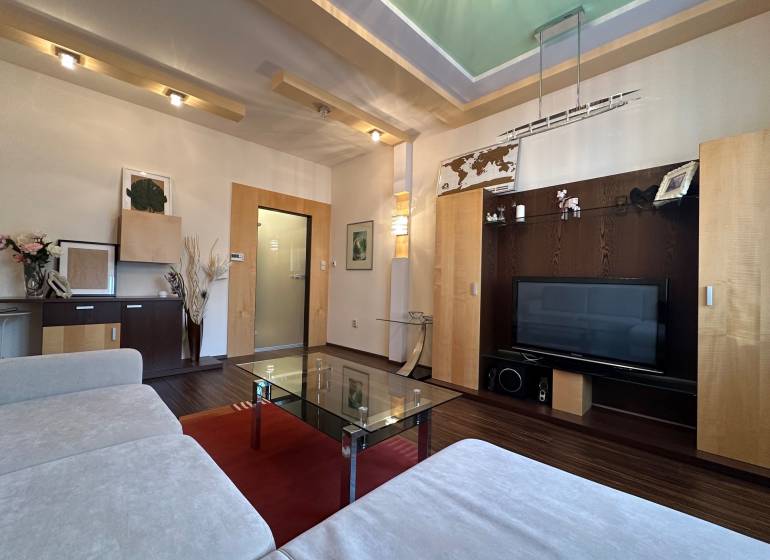Living room in a two-room apartment with a sofa, glass table, and television, floor with wood decor.