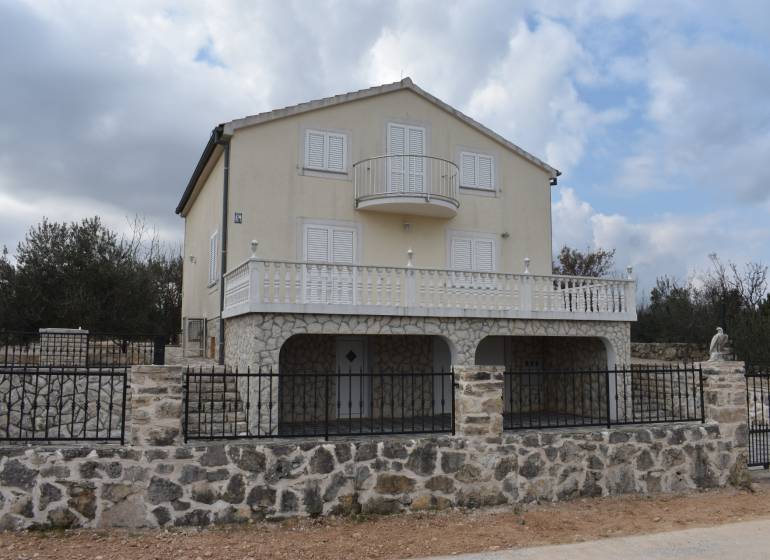 A family house in Pridraga with a stone facade and a balcony, surrounded by a stone fence.