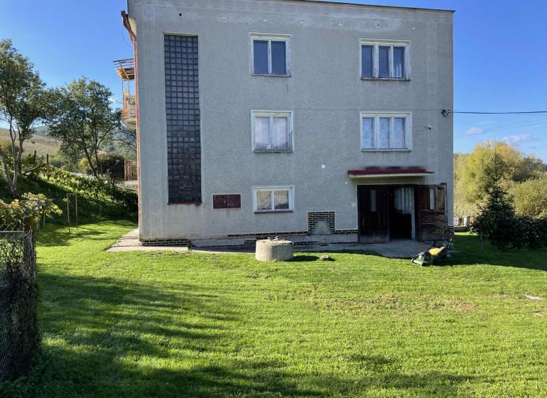 A family house in Hajnáčka with a lawn, trees, and garden tools in the yard.