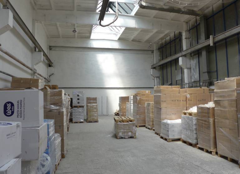 In the warehouse, pallets with cartons and crates are arranged on a concrete floor.
