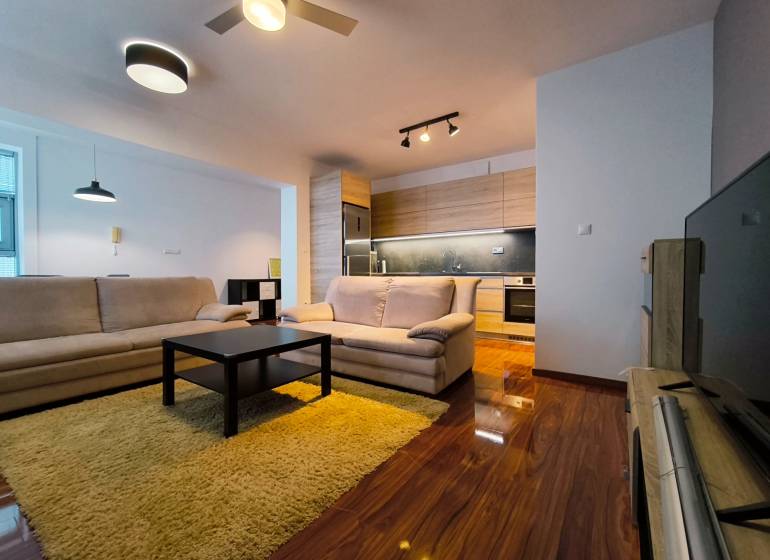 Living room in a two-room apartment with a wooden decor floor and neutral furniture.