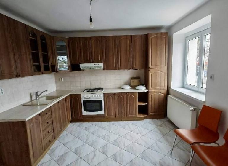 A kitchen with wooden cabinets, white walls, and orange chairs in a two-room apartment.