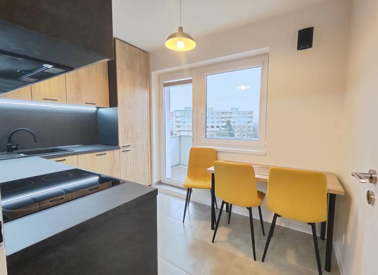 A kitchen in a studio apartment with a wood-patterned floor and yellow chairs.