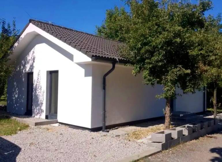 A family house in Kaplna with a white facade, a sloped roof, and greenery around.