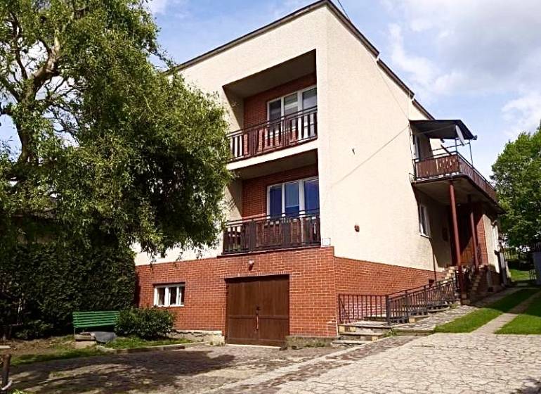 A family house in Nižná Myšľa with balconies, a tree, and a garage on a paved area.