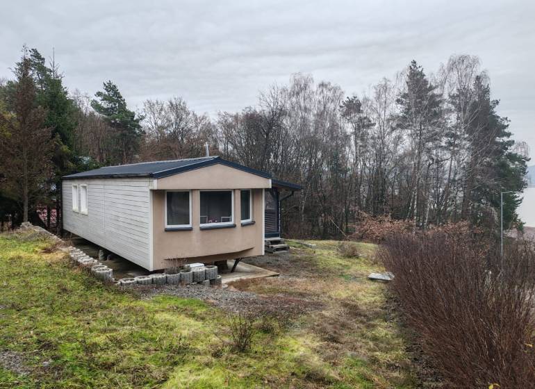 A wooden cottage on Main Street in Nova Kelca surrounded by trees and a grassy plot.