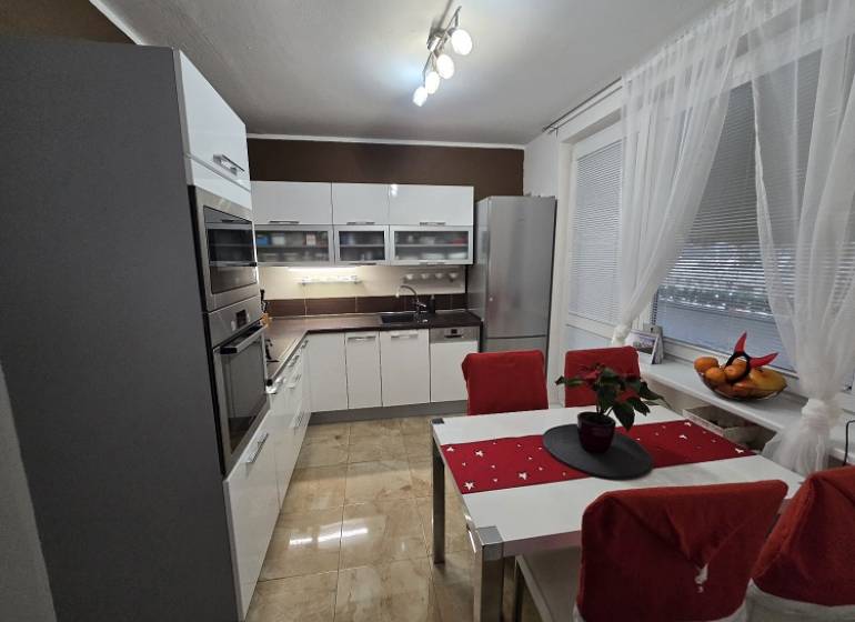 A kitchen in a 3-room apartment with glossy white cabinets, appliances, and a dining table.