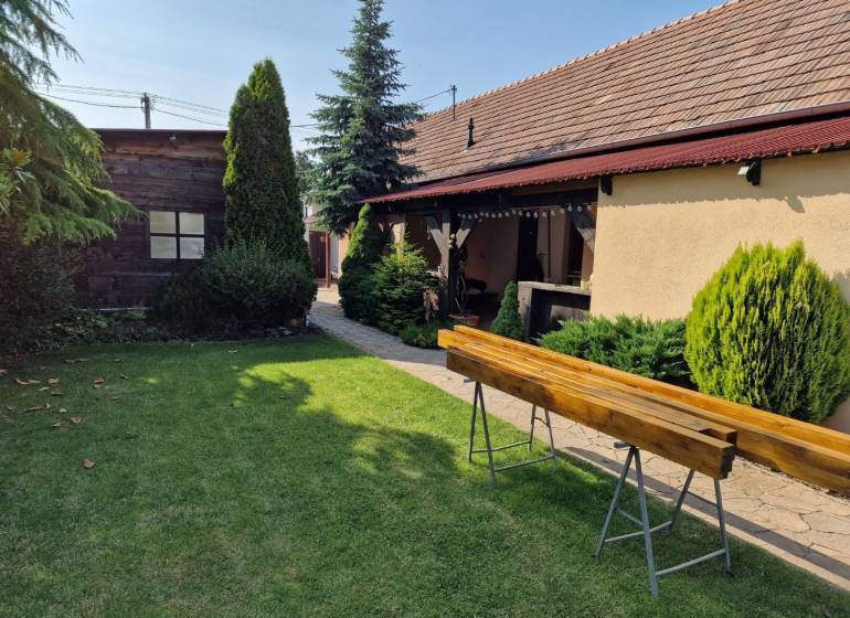 A family house in Dlhá nad Váhom with a lawn, bushes, and a wooden bench in the garden.