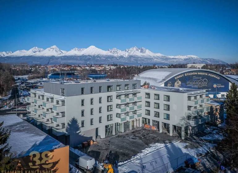 A building in Poprad with the snow-covered Tatras in the background and an ice rink.