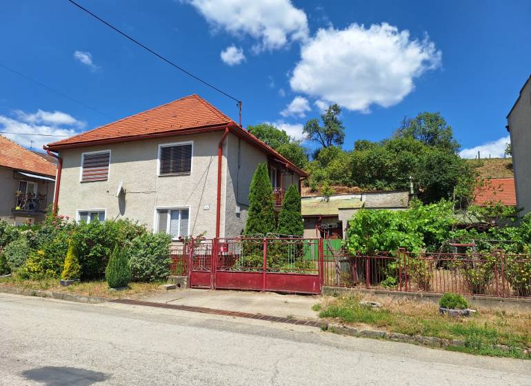 A family house in Tachtoch, with a red roof, fence, and garden in a green environment.