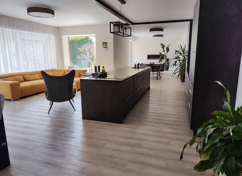 Kitchen and living room in a family house with an island, a yellow sofa, and a floor with a wooden decor.