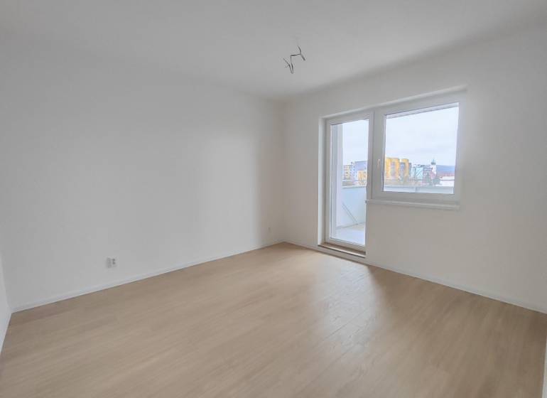 An empty room in a two-room apartment with a wood-patterned floor and balcony doors.