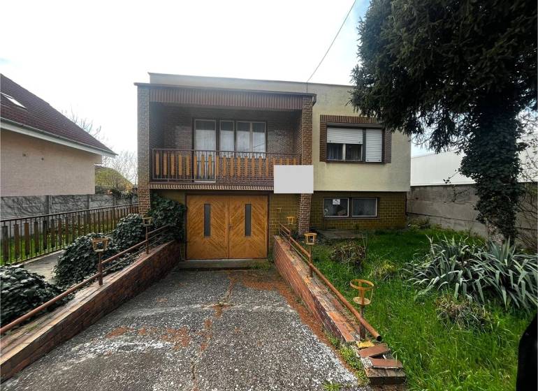 A family house in Šaľa with a garage, balcony, and garden, surrounded by vegetation and a fence.
