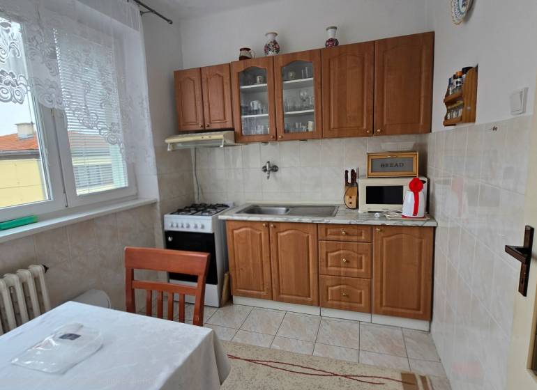 A kitchen in a 3-room apartment with a kitchen unit, stove, microwave, and table with a tablecloth.