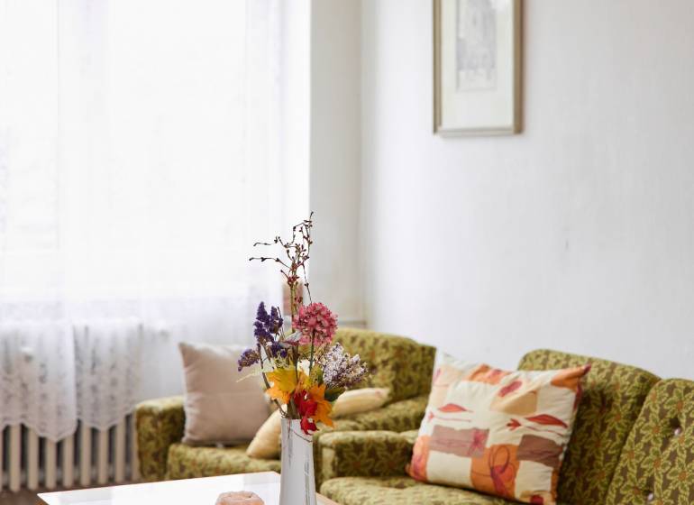 A bright living room in a three-room apartment with a sofa, table, and decorative flowers in a vase.