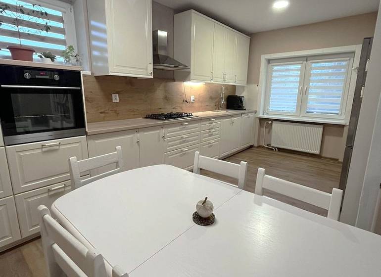 A kitchen in a family house with white furniture and a wooden decor floor.