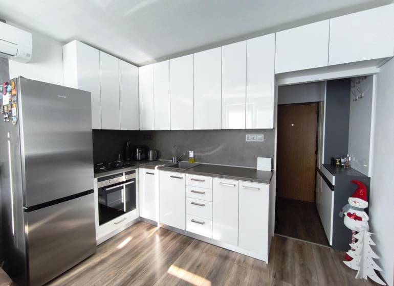 A kitchen with white cabinets and a wood-patterned floor in a studio apartment.