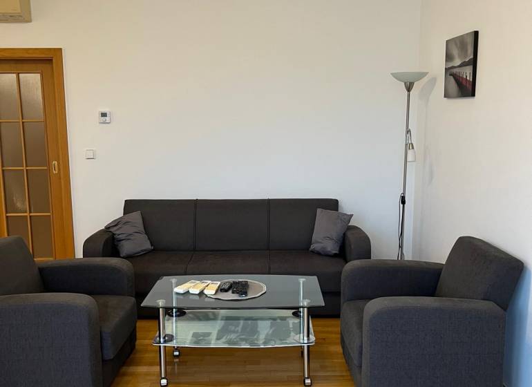 Gray sofa in a 3-room apartment with wood-patterned flooring and a glass table.