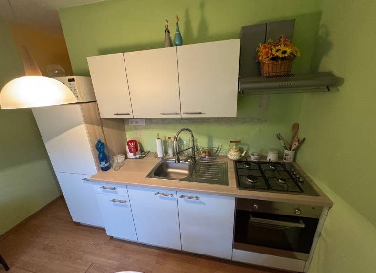 A kitchen in a studio apartment with white cabinets and a wood-patterned floor.