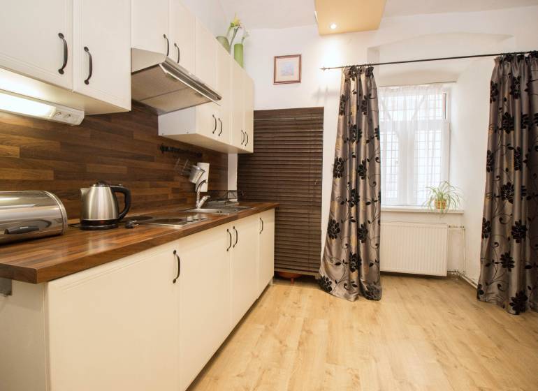 A kitchen with a wood-patterned floor in a 2-room apartment, white cabinets, and patterned curtains.
