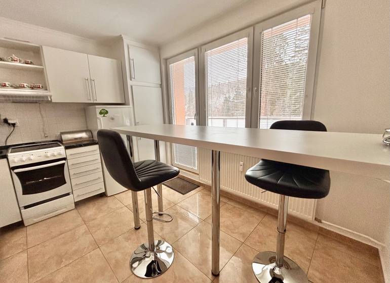A kitchen in a 2-room apartment with a bar table, chairs, and white kitchen cabinets.