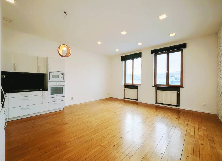Living area in a 2-room apartment with a kitchen unit and a wooden decor floor.