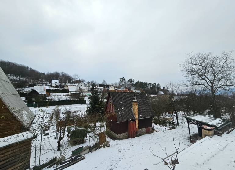 A snow-covered cottage in Lieskovec in Dubnica nad Váhom surrounded by trees and other cottages.