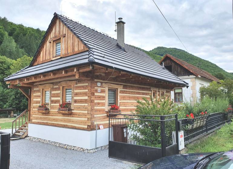 Wooden cottage on Hviezdoslavova Street in Tisovec surrounded by green hills.