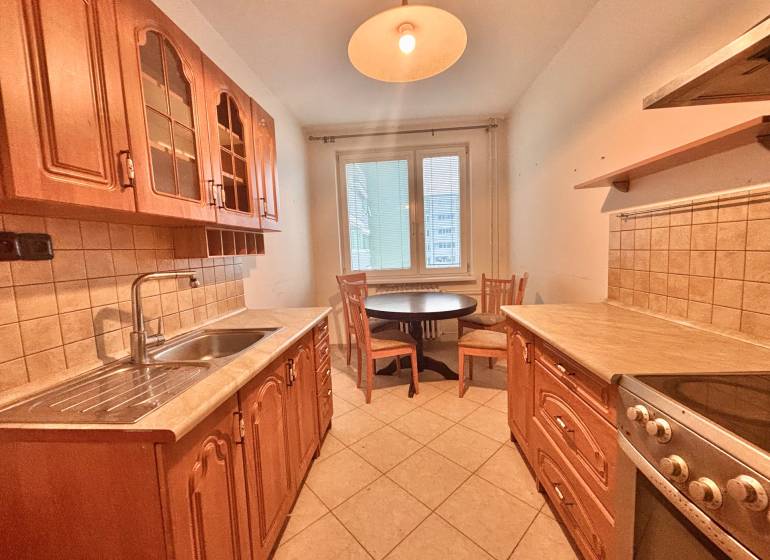 A kitchen in a 3-room apartment with brown cabinets, a dining table, and light tiles.
