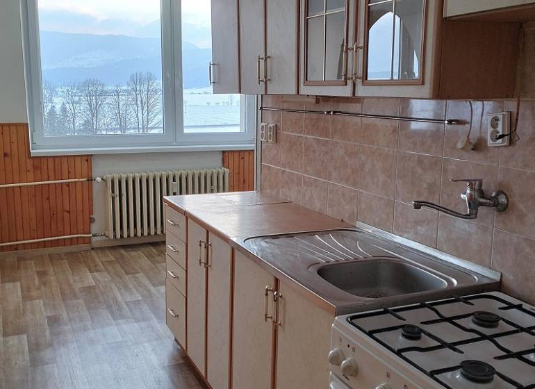 A kitchen in a 2-room apartment with a wooden decor floor and a view of nature.
