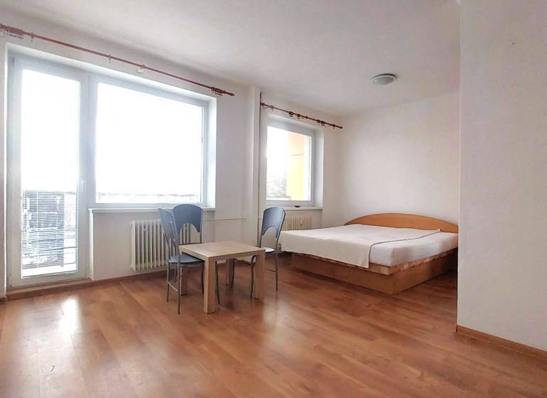 A studio apartment with a bed, table, chairs, and a wooden decor floor.