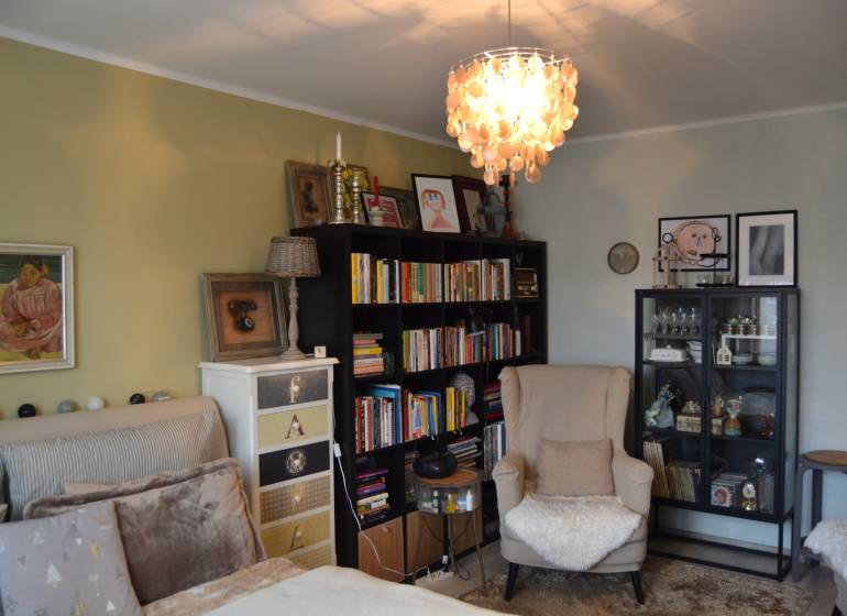 A room in a three-room apartment with an armchair, a bookshelf, chandeliers, and wall decorations.