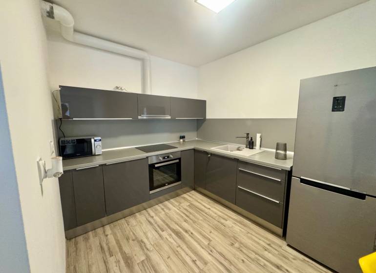 A kitchen in a 2-room apartment with a wood-patterned floor and a gray kitchen unit.