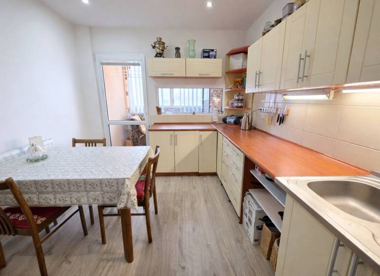 A kitchen in a 3-room apartment with white furniture and a wooden decor floor.