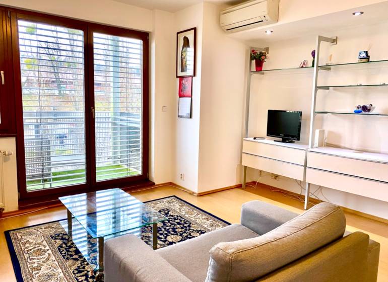 Living room in a 2-room apartment with an armchair, a glass table, and a floor with a wood decor.