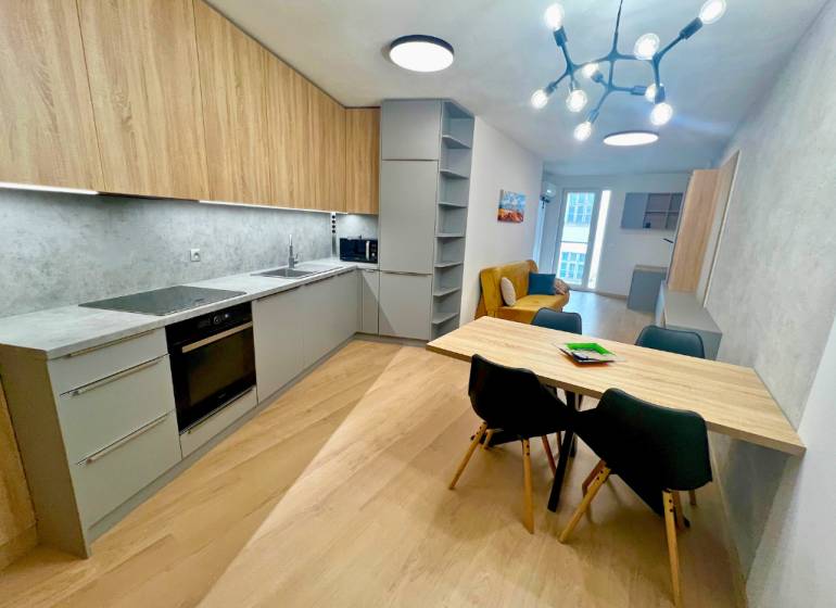 A kitchen in a two-room apartment with a wooden decor floor and a dining table.