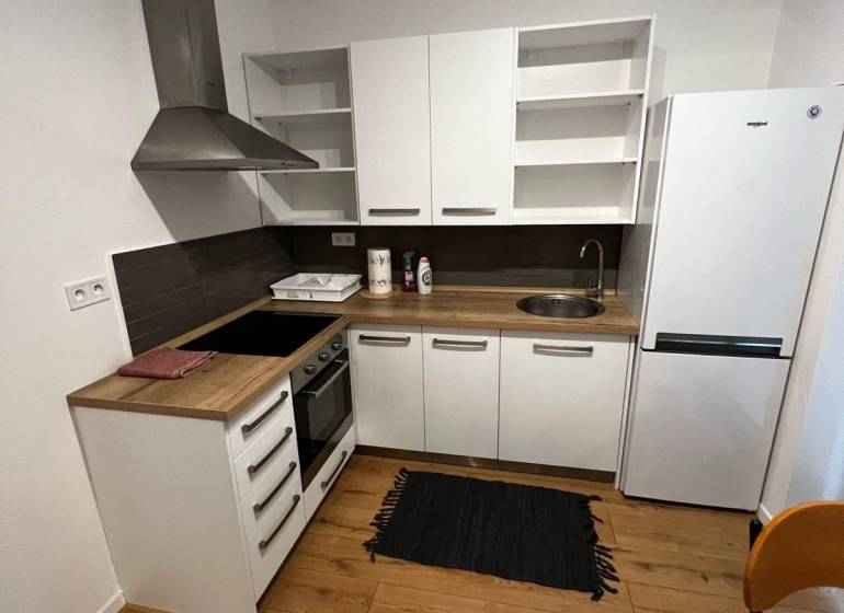 The kitchen in the 2-room apartment on Brečtanová Street with wooden flooring and white furniture.