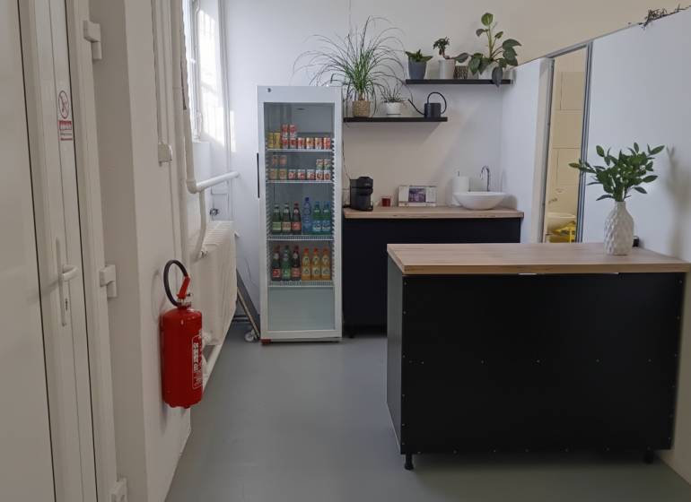 A small kitchenette in the warehouse and hall area with a refrigerator and plants.