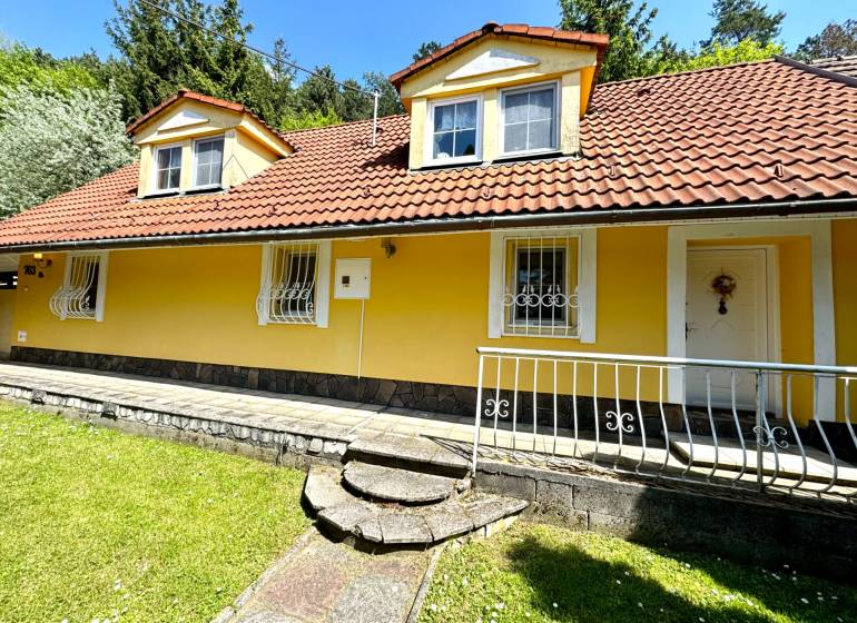 A family house in Vrbovce with a yellow facade, a red roof, and a front garden.