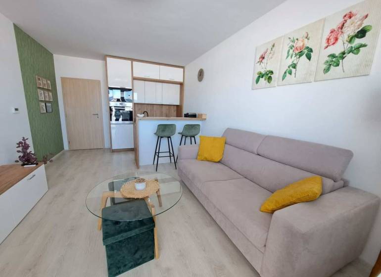 Studio apartment with wood-patterned flooring, a sofa, and bar stools.