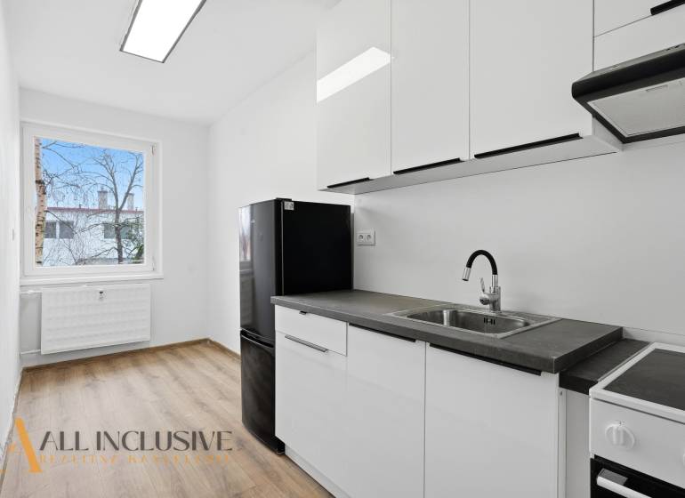 A kitchen in a 3-room apartment with a black refrigerator and a wooden decor floor.