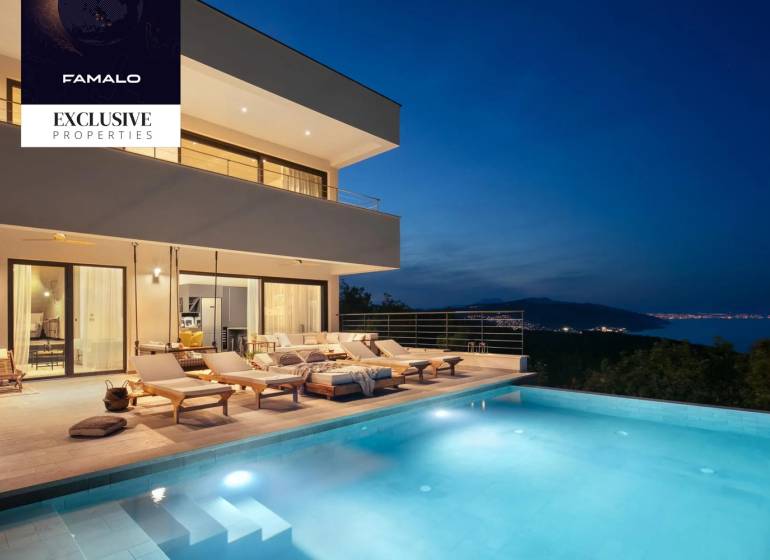 Villa with a terrace and pool, with a night view of the illuminated coastline.