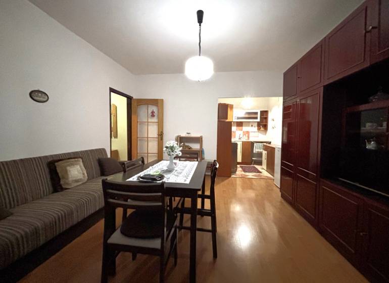 A two-room apartment with a wooden floor, a dining table, and a kitchen in the background.