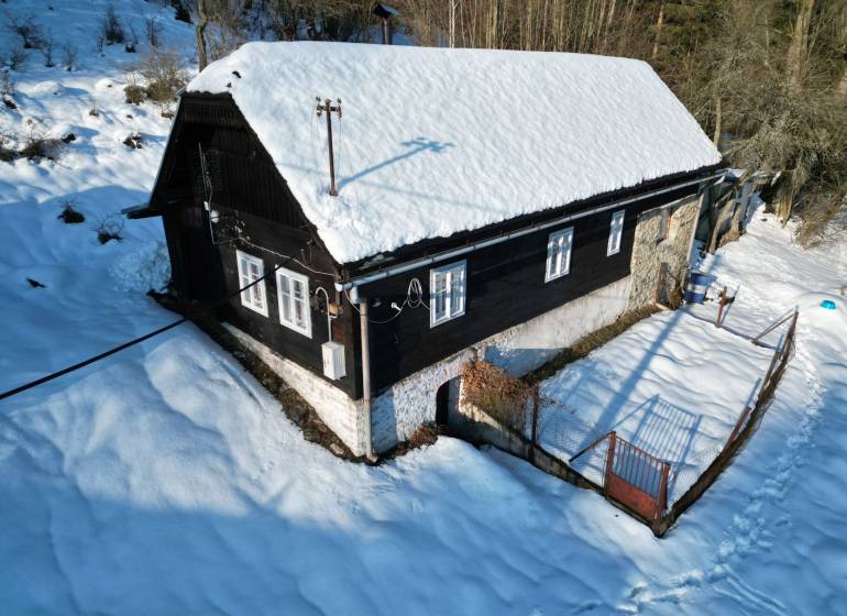 A snow-covered cottage in Veľké Rovné surrounded by a winter landscape and trees.