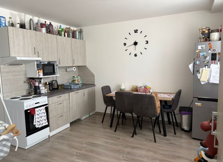 The kitchen of a 2-room apartment with a wooden decor floor, a dining table, and a kitchen unit.